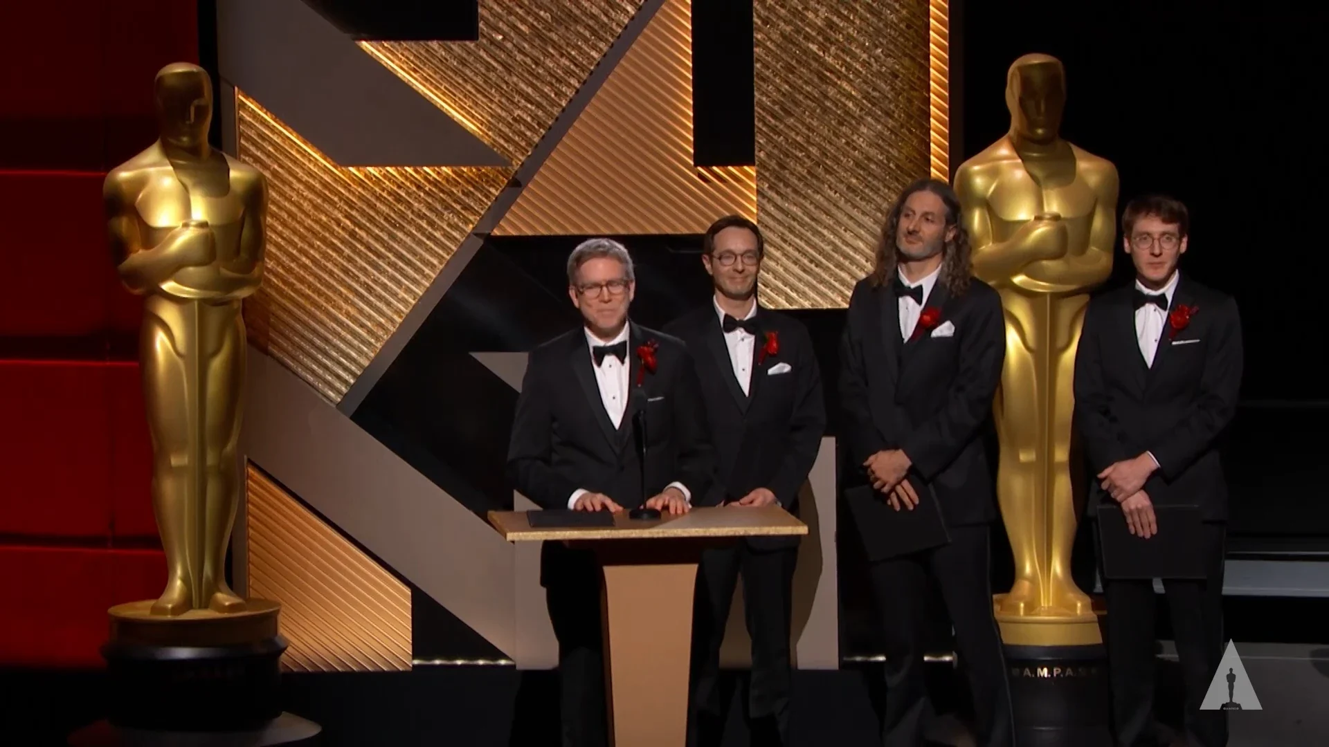 The Substance team on stage in tuxedos at the 2023 Scientific and Technical Awards, one speaking at the podium, between two Oscar statues.